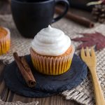 A pumpkin spice cupcake with cinnamon frosting next to a wooden fork.