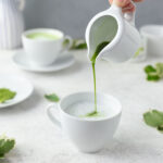 Pouring matcha tea into teacup filled with warm coconut milk