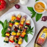 Vegetable and tofu skewers next to a dish of chili honey marinade