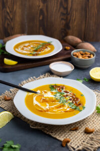 Sweet potato and leek soup in a white plate with a black spoon on the side