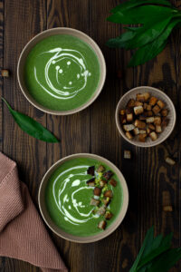 Two bowls of vegan coconut wild garlic soup on a dark wooden surface
