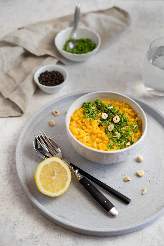 Carrot risotto with hazelnut gremolata topping next to a lemon wedge and cutlery