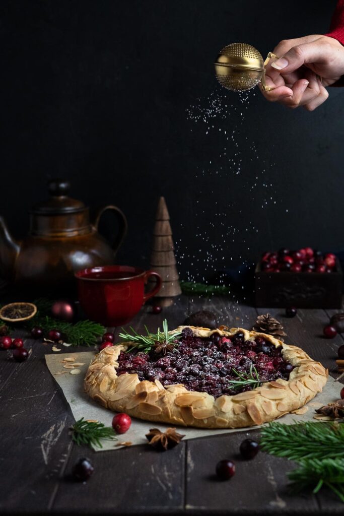 Dusting Vegan Cranberry Apple Galette with powdered sugar