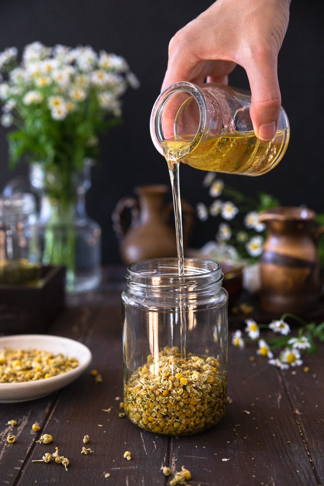Pouring almond oil over dried chamomile flowers