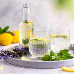 Two glasses of lemon balm lemonade next to a bottle of lemon balm syrup