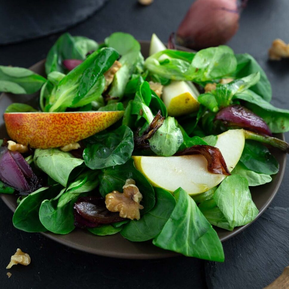 Autumn salad with lambs lettuce, pears, onions and walnuts on a dark brown plate.