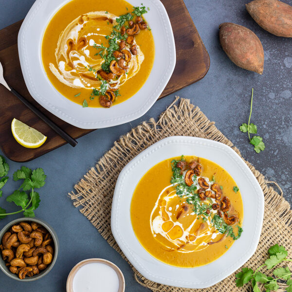 Two bowls of sweet potato and leek soup garnished with curried cashews, coriander, cream and oil