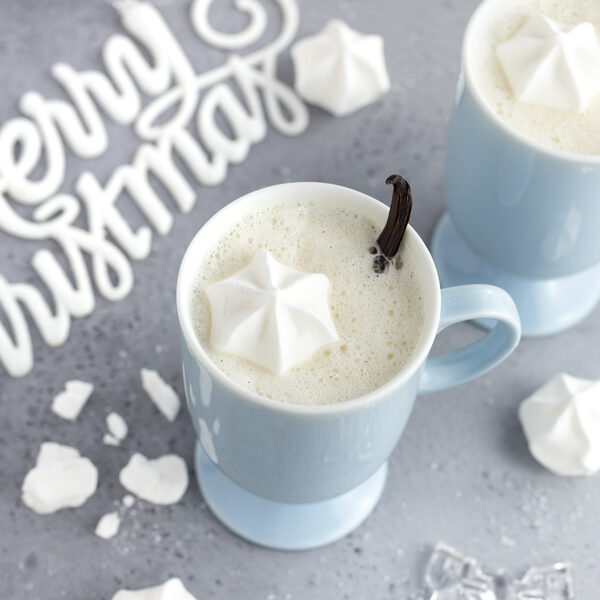 A cup of warm vanilla milk with a meringue kiss and vanilla bean garnish.